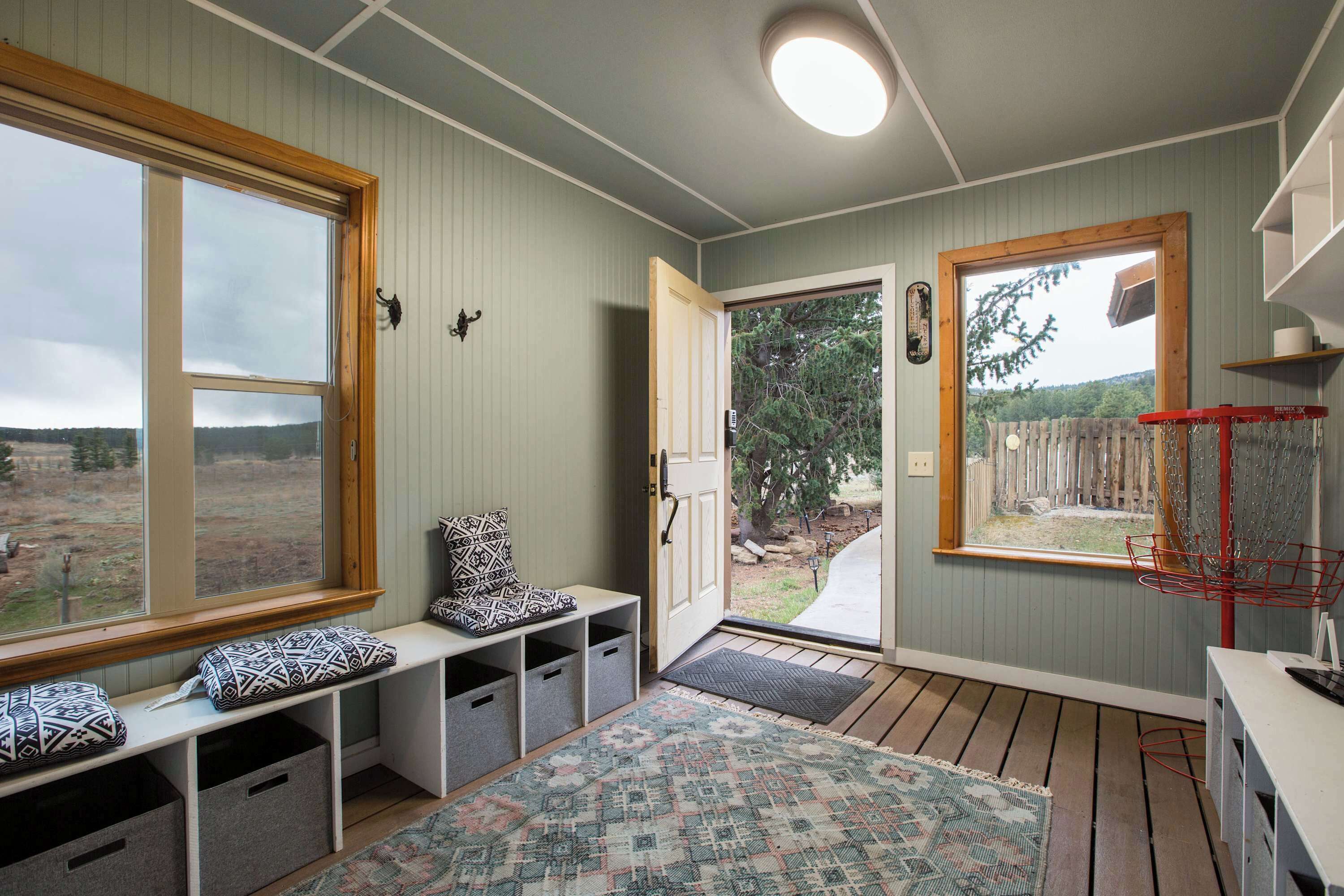 Una habitación con un banco, una puerta que da al exterior, una ventana y un estante pequeño.