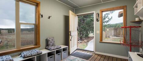 Una habitación con un banco, una puerta que da al exterior, una ventana y un estante pequeño.