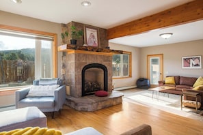 Una sala de estar con chimenea de piedra, vigas de madera, un sofá y un ventanal grande.