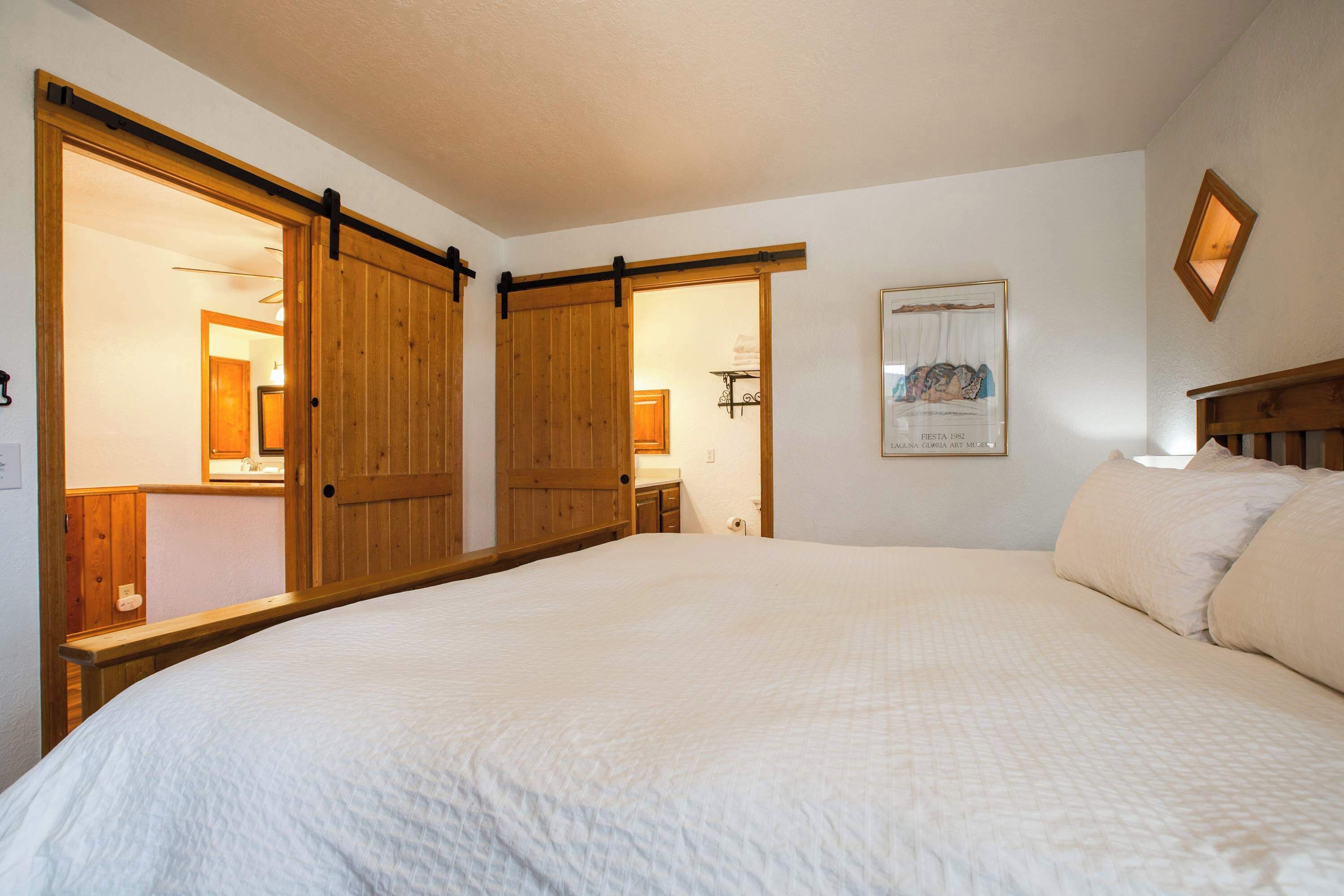 Un dormitorio con una cama grande, un armario de madera y un baño visible a través de una puerta abierta.