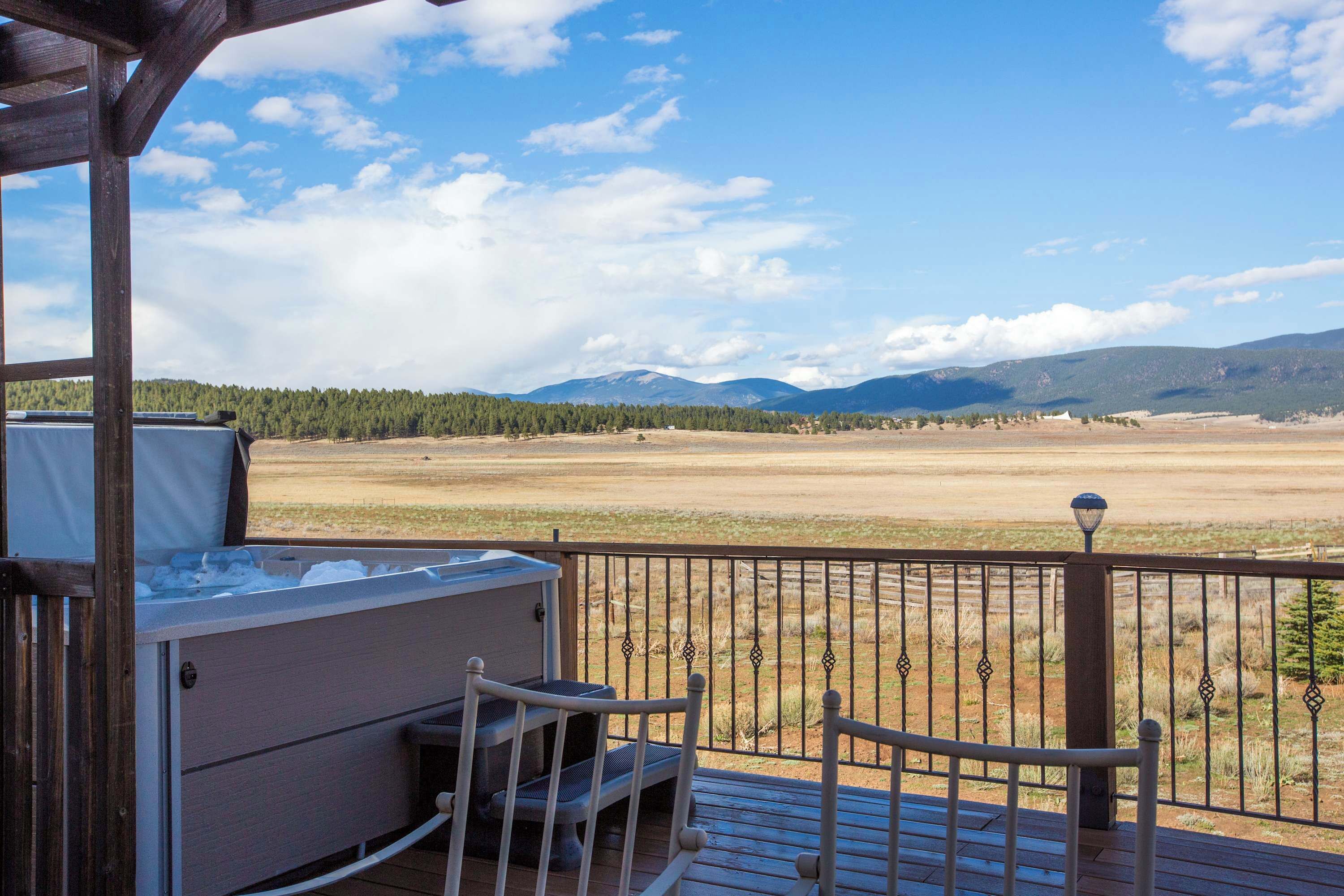 A wooden deck with a hot tub, a grill, and a view of a mountainous landscape.