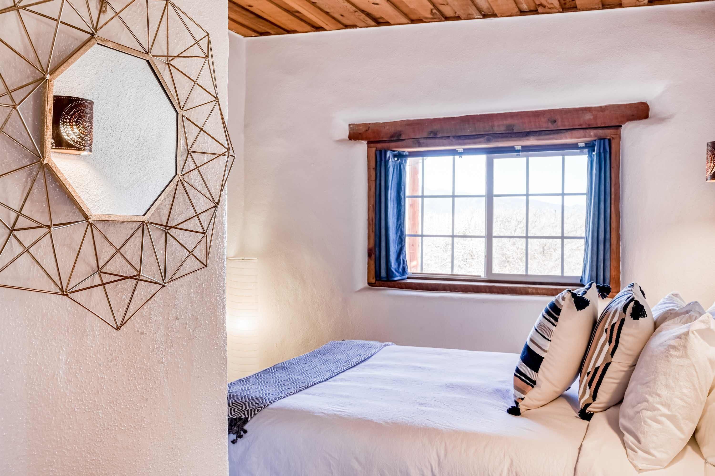 Un dormitori amb una decoració mural geomètrica, una finestra amb cortines blaves i un llit amb almoçades estampades.