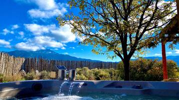 A hot tub with a waterfall feature, surrounded by trees and a mountain backdrop.