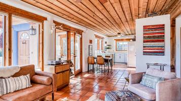 A spacious living area with a wooden ceiling, a dining area, and a kitchen in the background.
