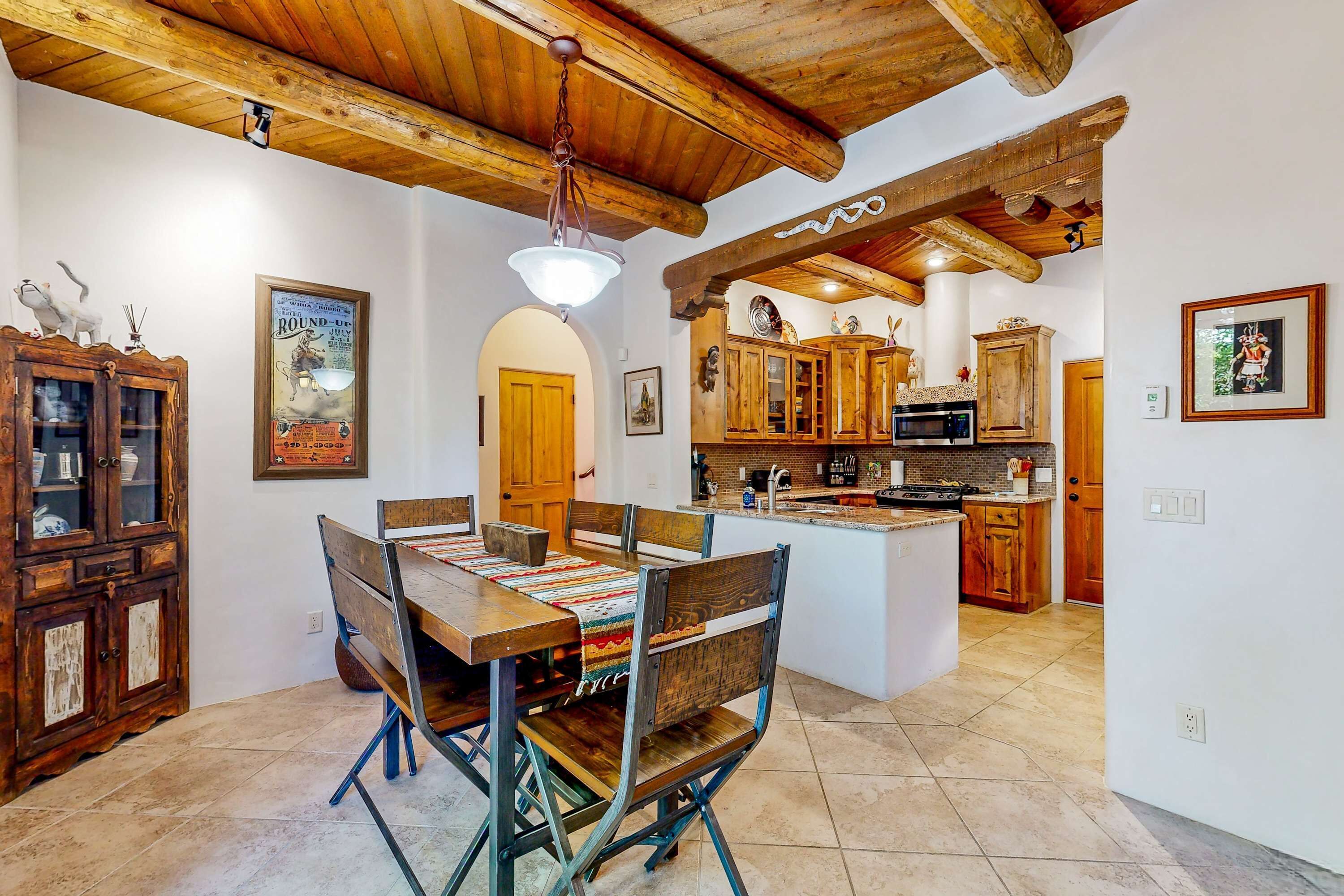 Zona pranzo con tavolo e sedie in legno, cucina con mobili in legno e lampadario.
