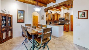 Uma área de refeições com mesa e cadeiras de madeira, uma cozinha com armários de madeira e um lustre.