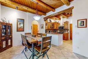 Un coin repas avec une table et des chaises en bois, une cuisine avec des meubles en bois et un luminaire suspendu.