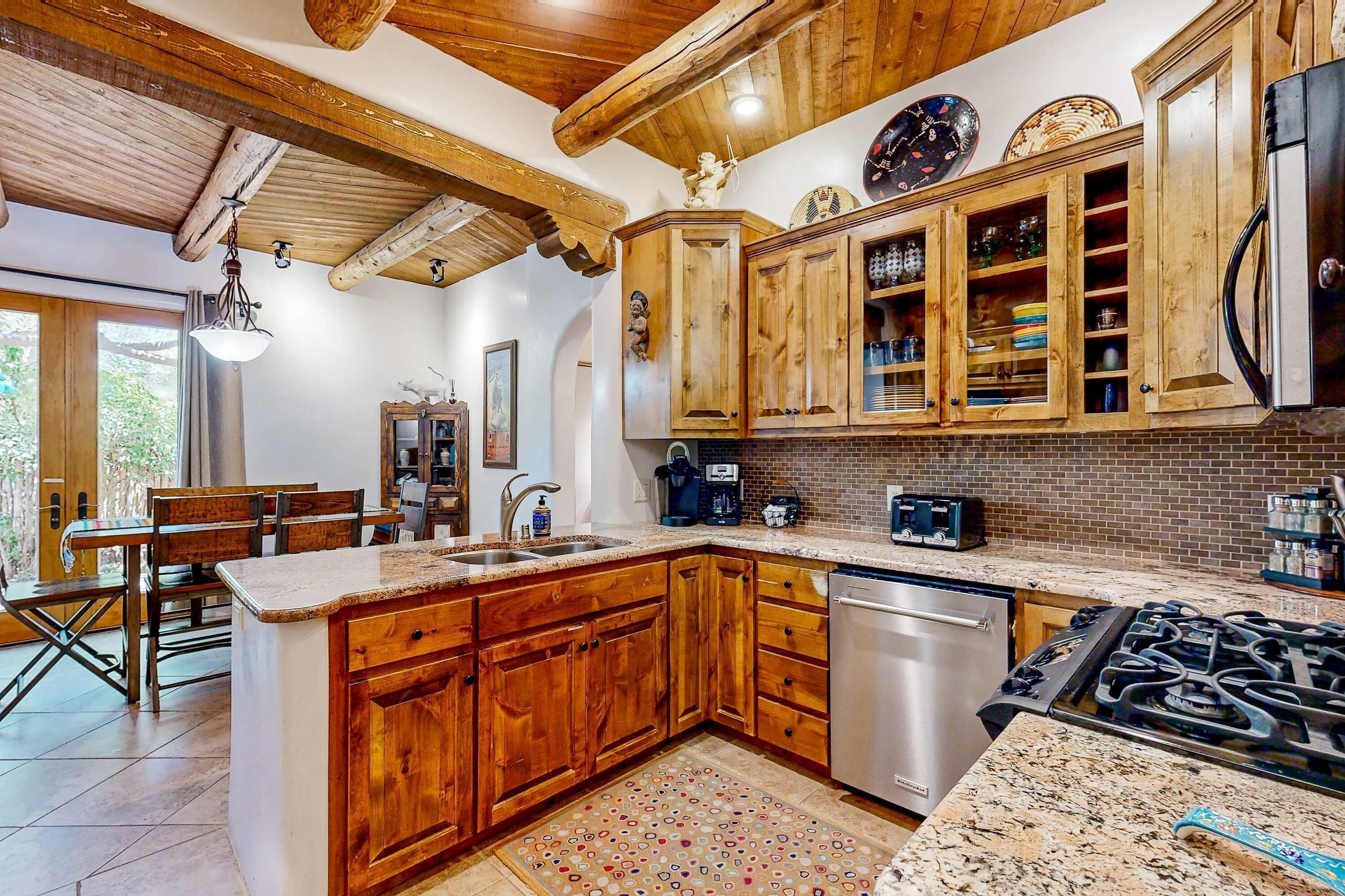 A kitchen with wooden cabinets, a granite countertop, a dishwasher, a stove, and a dining area with a table and chairs.