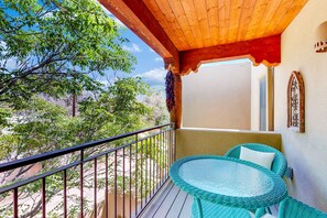 Un balcon avec une table et des chaises en osier, un plafond en bois et une vue sur les arbres.