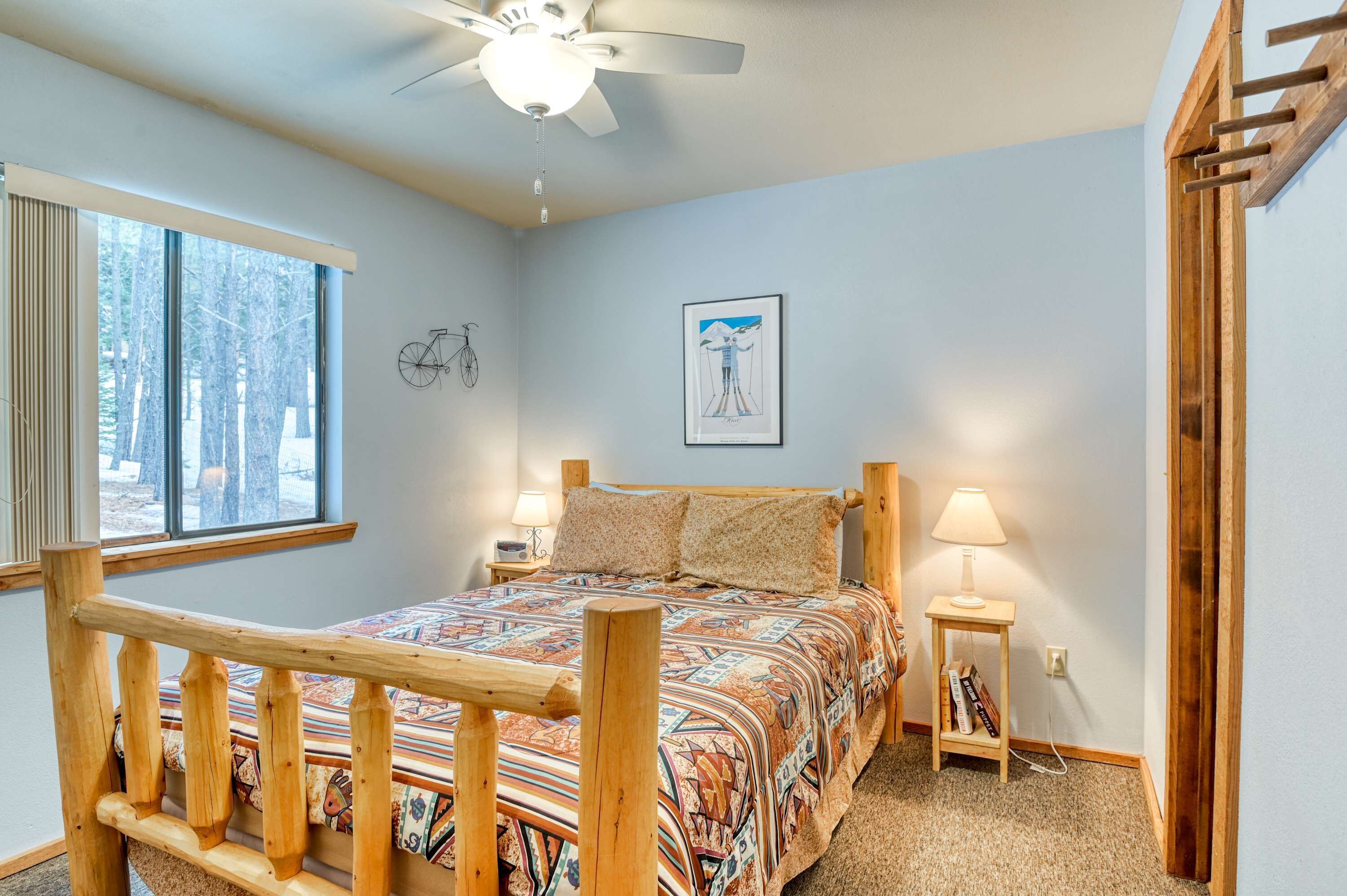 A bedroom with a wooden bed, a ceiling fan, a window with a view of trees, and a wall-mounted bicycle.
