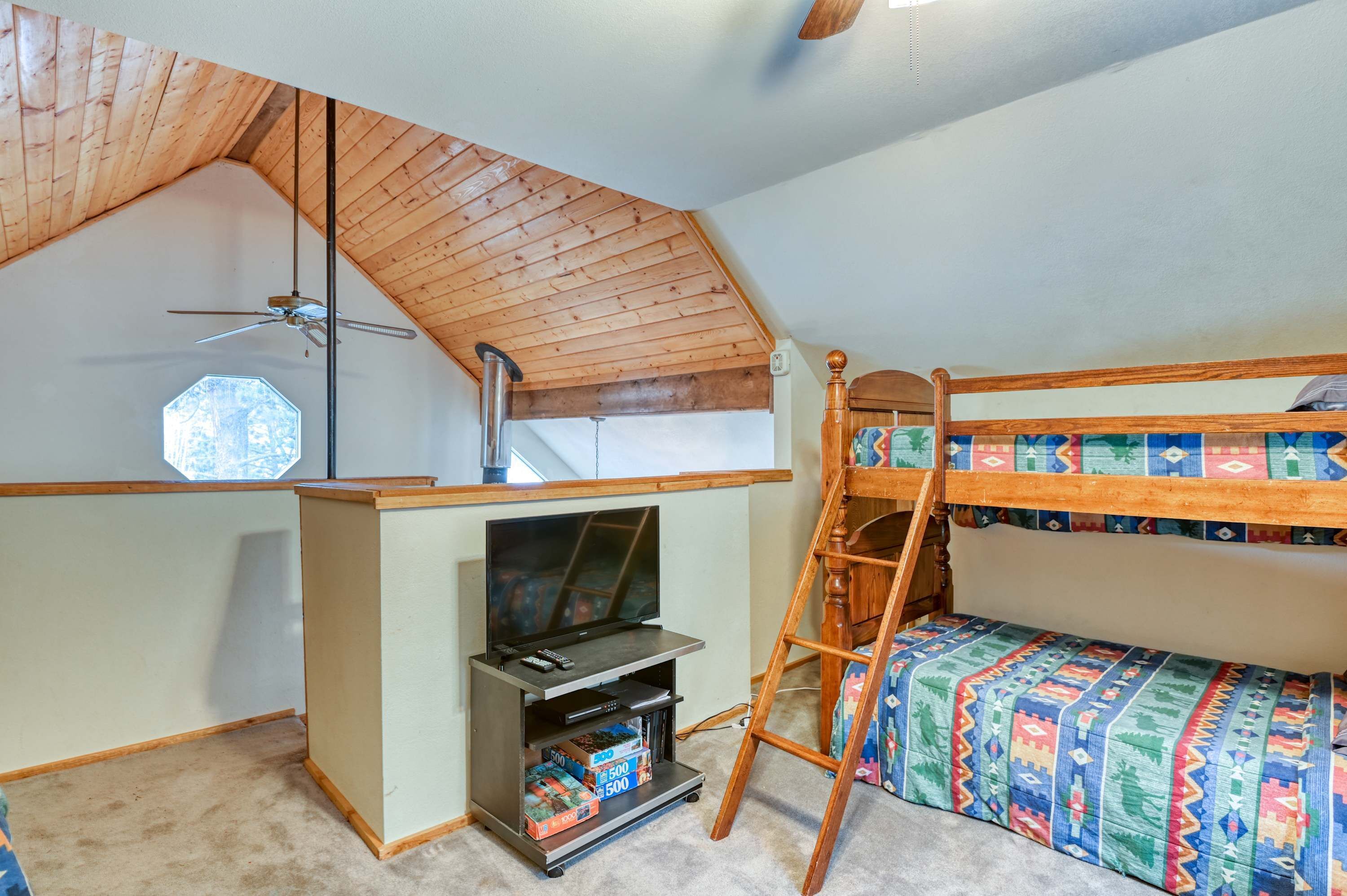Un dormitorio con techo inclinado, una cama litera, un mueble para televisión con juegos y una escalera.