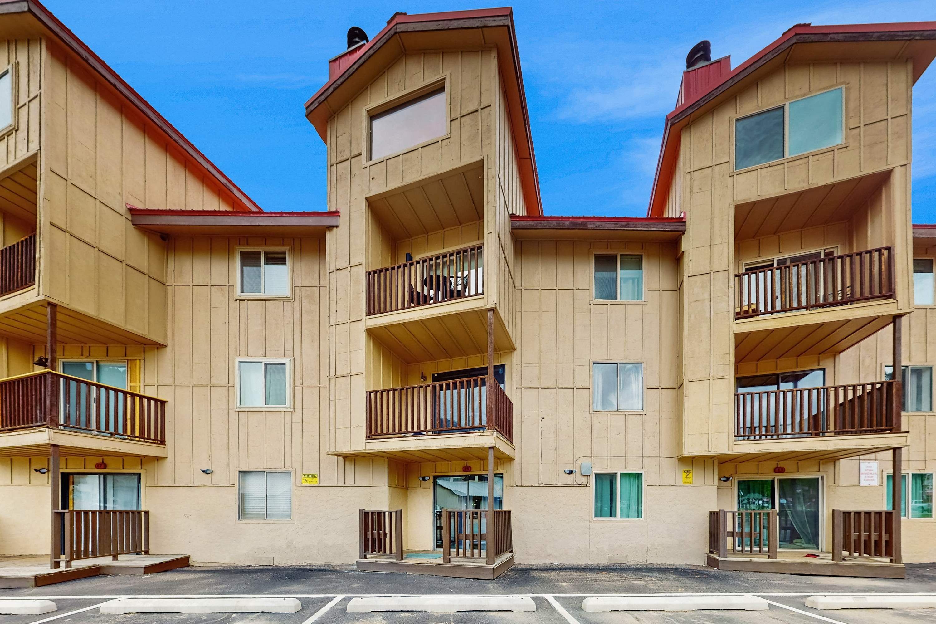 A multi-story building with balconies, a central entrance, and a parking lot.