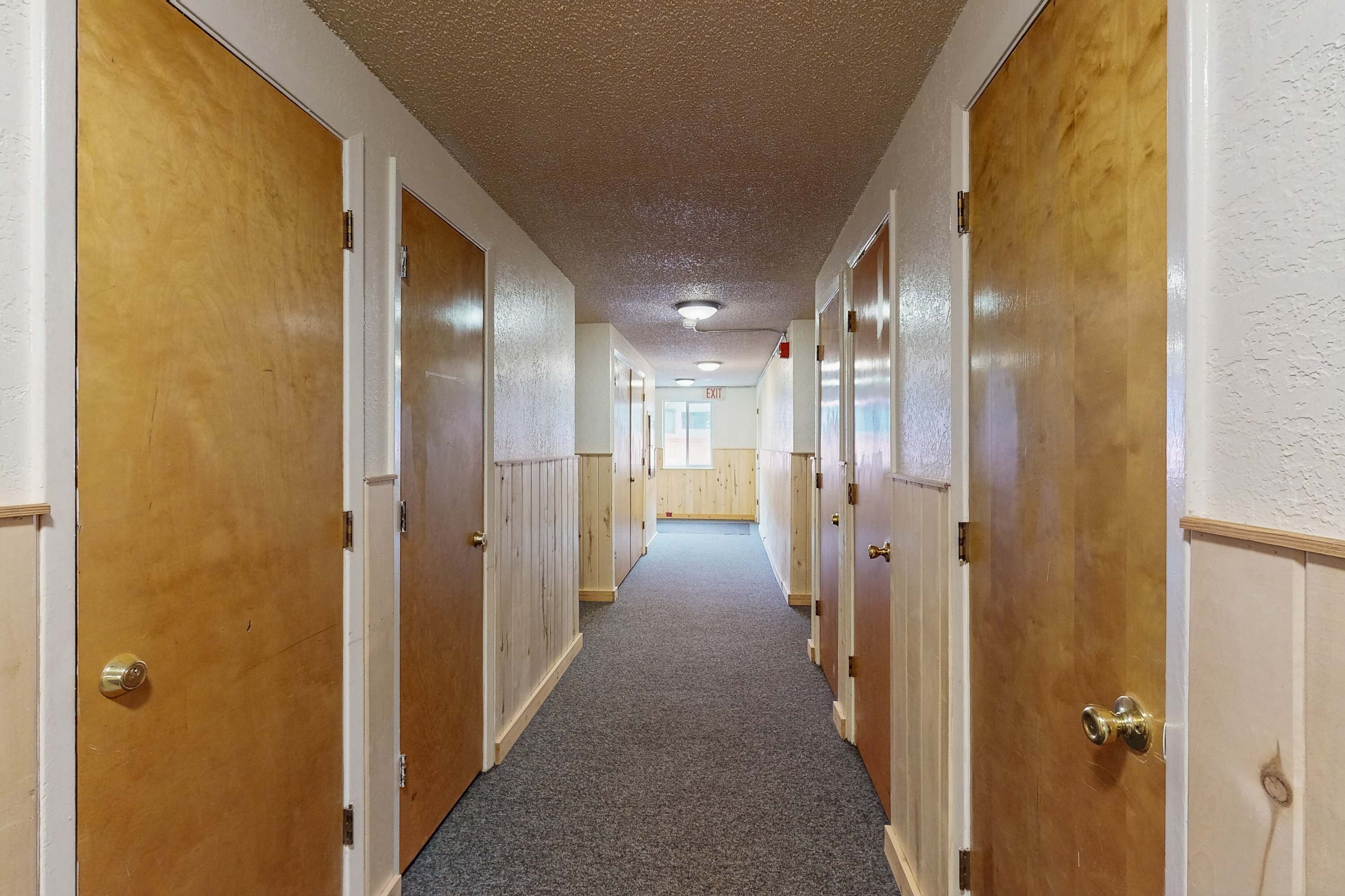 A hallway with wooden doors, carpeted floor, and a ceiling with recessed lighting.
