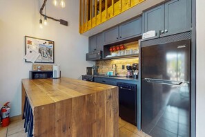 A modern kitchen with a wooden island, stainless steel appliances, and a hanging light fixture.