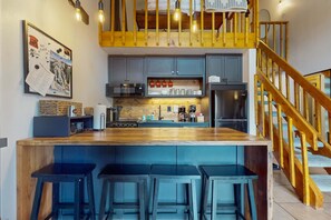 A modern kitchen with a wooden island, bar stools, a microwave, and a refrigerator.