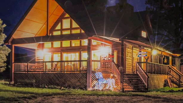 A lodge with a prominent triangular roof, a porch with a railing, and a staircase leading to the entrance. - Painted Pony Cabin - Wraparound Deck in the Pines (Angel Fire)