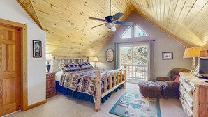 A bedroom with a wooden ceiling, a bed with patterned bedding, a desk with a lamp, and a view of the outdoors. - Painted Pony Cabin - Wraparound Deck in the Pines (Angel Fire)
