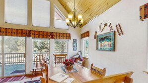 A wooden dining table with chairs, a chandelier, and a view of the outdoors. - Painted Pony Cabin - Wraparound Deck in the Pines (Angel Fire)