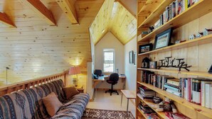 A cozy cabin interior with a wooden ceiling, a sofa, a desk with a computer, and a bookshelf filled with books. - Painted Pony Cabin - Wraparound Deck in the Pines (Angel Fire)