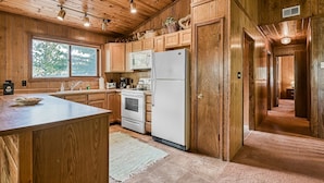 A wooden cabin-style kitchen with a large island, built-in appliances, and a view through a window.