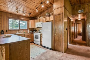 A wooden cabin-style kitchen with a large island, built-in appliances, and a view through a window.