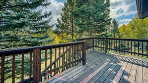 A wooden deck with a railing, surrounded by trees and a clear sky.