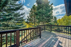 A wooden deck with a railing, surrounded by trees and a clear sky.