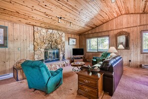 A wooden-paneled room with a stone fireplace, a television, a sofa, and a lamp.