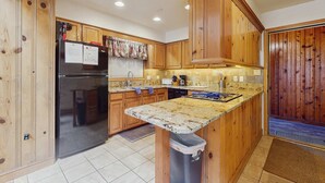 Una cucina con mobili in legno, un frigorifero nero, un piano di lavoro in granito e un cestino.