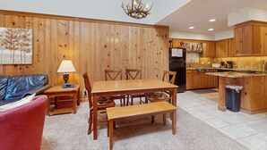 Un'area pranzo con tavolo e sedie in legno, un lampadario e una cucina sullo sfondo.