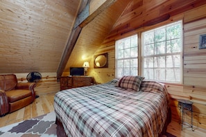 A cozy cabin bedroom with a bed, a chair, a dresser, and a window.