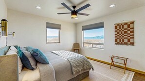 Ein Schlafzimmer mit Bett, Deckenventilator, Fenstern und einer Wanddecke mit Karomuster.