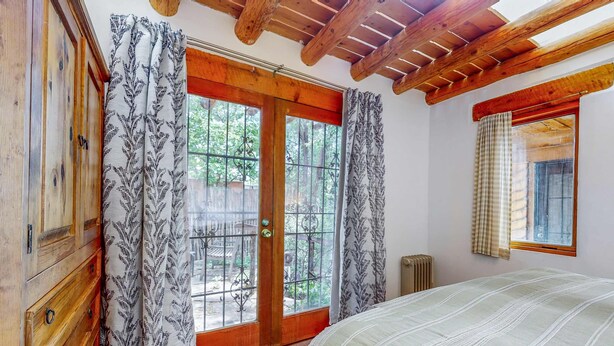 A bedroom with a wooden ceiling, a bed, a window with curtains, and a view of greenery outside. - Casa Oeste - Walk to Plaza, Shaded Patio, Dog OK (Santa Fe)