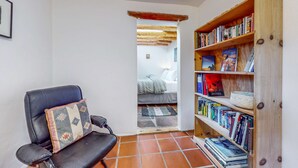 A room with a black leather chair, a wooden bookshelf, a tiled floor, and a doorway leading to another room. - Casa Oeste - Walk to Plaza, Shaded Patio, Dog OK (Santa Fe)
