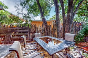 An outdoor seating area with a glass-top table and metal chairs, surrounded by trees and a wooden fence. - Casa Oeste - Near Plaza with Santa Fe Charm (Santa Fe)