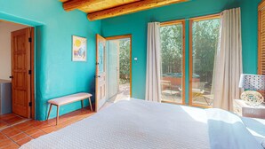A bedroom with a large bed, a bench, a door, and a view through a sliding glass door.