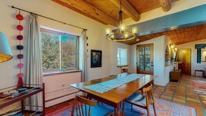 A dining area with a wooden table, chairs, a chandelier, and a view of the outdoors through a window.