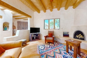 A living room with a TV, a fireplace, a sofa, a chair, and a patterned rug. - Casa del Suenos - Steps to Plaza - Patio & Garden (Taos)