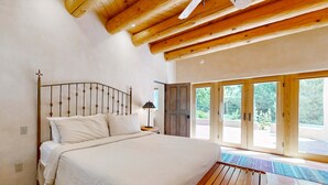 Een slaapkamer met een bed, houten balken in het plafond, een nachtkastje en uitzicht door grote glazen deuren.