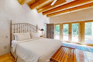 A bedroom with a bed, wooden ceiling beams, a nightstand, and a view through large glass doors. - Casa del Suenos - Steps to Plaza - Patio & Garden (Taos)