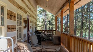 Un portico coperto con travi in legno, un barbecue, posti a sedere all'aperto e vista su una foresta.