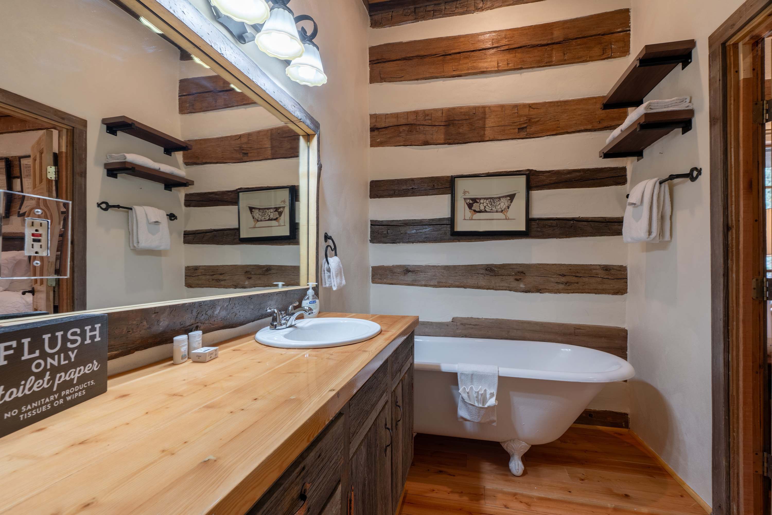 A bathroom with a wooden vanity, a white sink, a bathtub, and a sign indicating the use of toilet paper only.
