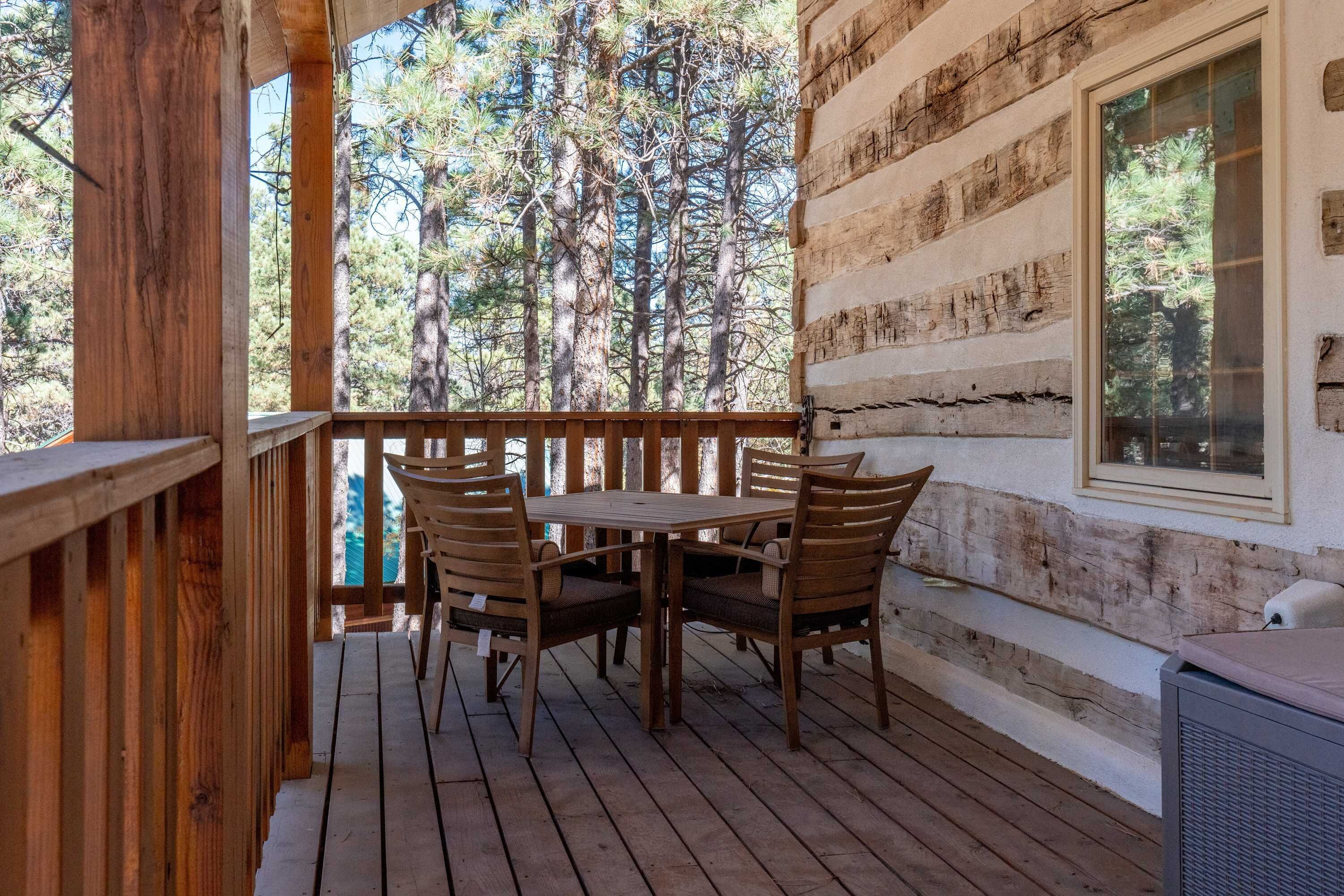 Terraza de madera con mesa y sillas, con vista a un bosque.