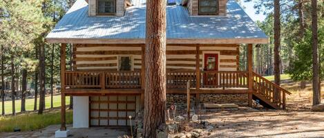 A log cabin with a porch, two windows, and a garage.