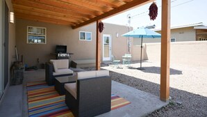 Une terrasse couverte, aménagée avec des meubles en osier, un barbecue et un parasol bleu.