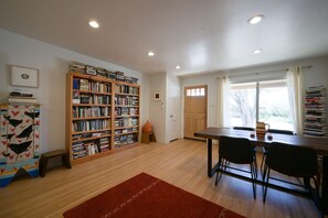 Ein Zimmer mit einer Holzregal, einem Esstisch mit Stühlen, einem kleinen Hocker und einem Fenster mit Vorhängen.