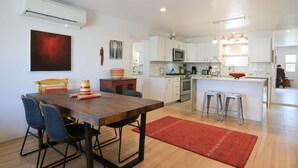 Une cuisine moderne avec des meubles blancs, un four à micro-ondes et un évier. On y trouve également un coin repas avec une table en bois et des chaises bleues.