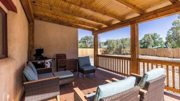 A covered outdoor patio with wicker furniture, a grill, and a view of the surrounding landscape.