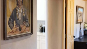 A framed portrait on a wall, a doorway leading to another room, and a glimpse of a kitchen area in the background. - Medina Casita - Mountain Views, Firepit, Pets Okay (El Prado)