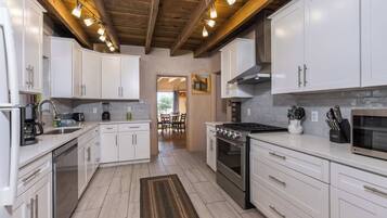 A modern kitchen with white cabinets, stainless steel appliances, and a wooden ceiling.